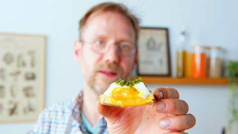 Pochiertes Ei auf einem Toast in einer Hand gehalten