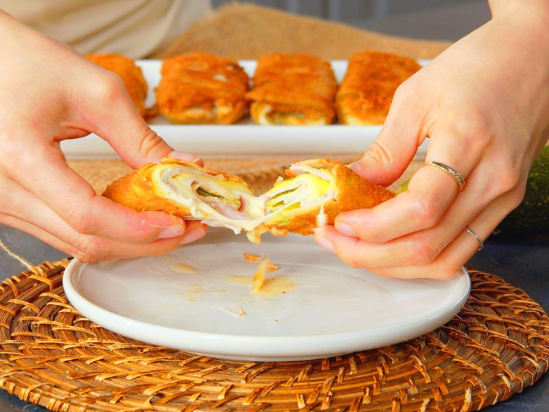 Eine Köchin hält eine Servierplatte mit drei panierten Zucchini-Cannelloni.