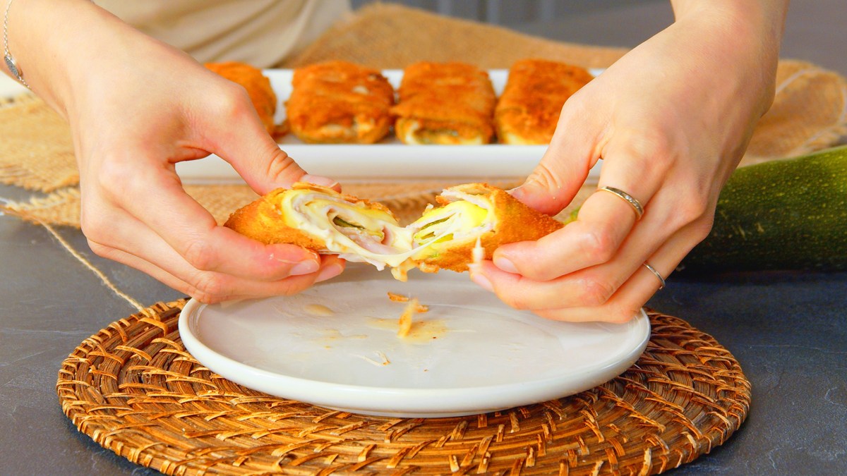 Eine Köchin hält eine Servierplatte mit drei panierten Zucchini-Cannelloni.