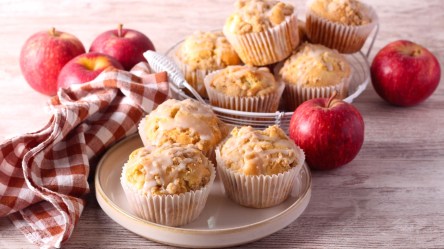 Mehrere Apfelmuffins mit Sour Cream auf zwei Tellern. Daneben liegen frische Äpfel.