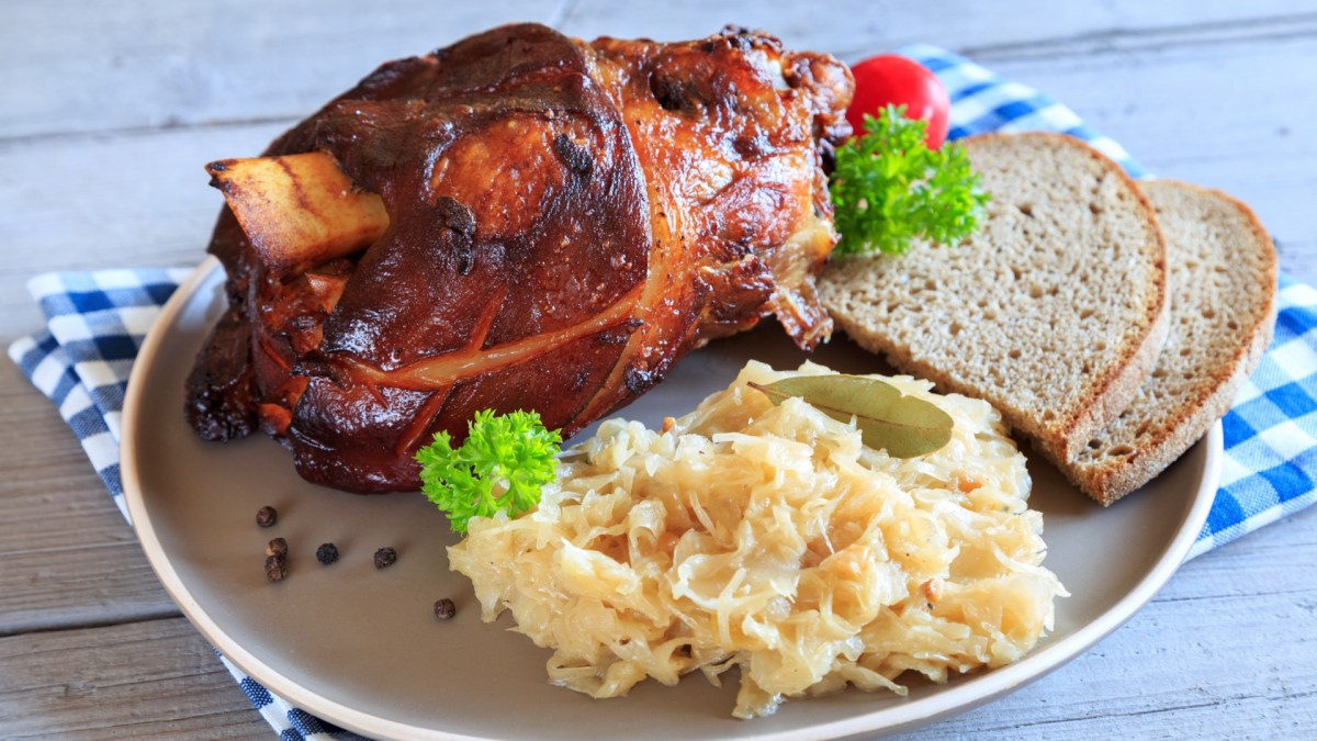 Eine bayerische Schweinshaxe mit Sauerkraut und Brotscheiben auf einem Teller.