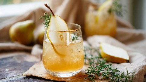 Ein Glas Birnen-Ingwer-Lillet mit Zimt. Rosmarinzweige und Birnenstücke sind zu sehen.