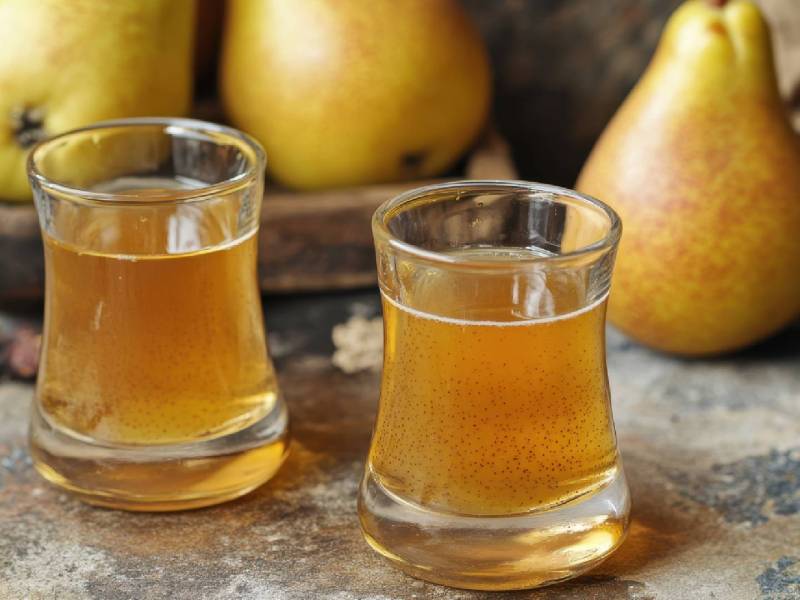 Zwei Schnapsgläser mit selbst gemachtem Birnenlikör auf einem Tisch, frische Birnen dahinter