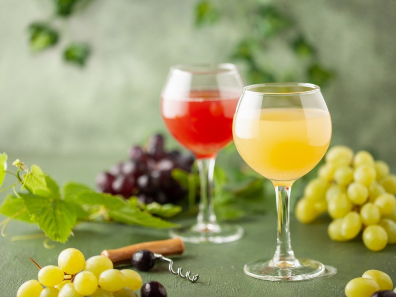 Zwei Gläser mit Federweißer und Federroter sind zu sehen. Darum liegen helle und dunkle Weintrauben.