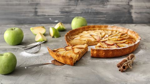 Eine Haferflocken-Apfel-Tarte mit einigen Äpfeln auf einer Arbeitsfläche.