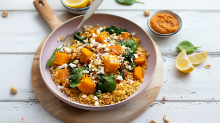 Hirsepfanne mit Kürbis, Spinat und Feta, angerichtet in einer Pfanne, die auf einem Holzbrett steht.