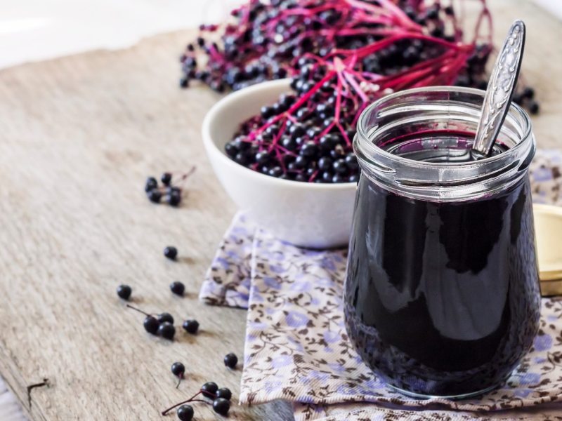 Ein Glas Holunderbeersaft. Daneben eine Schale mit Holunderbeeren.