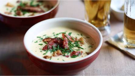 Schale mit Käse-Bier-Suppe mit Speck und Croûtons auf einem Tisch, Glas Bier daneben