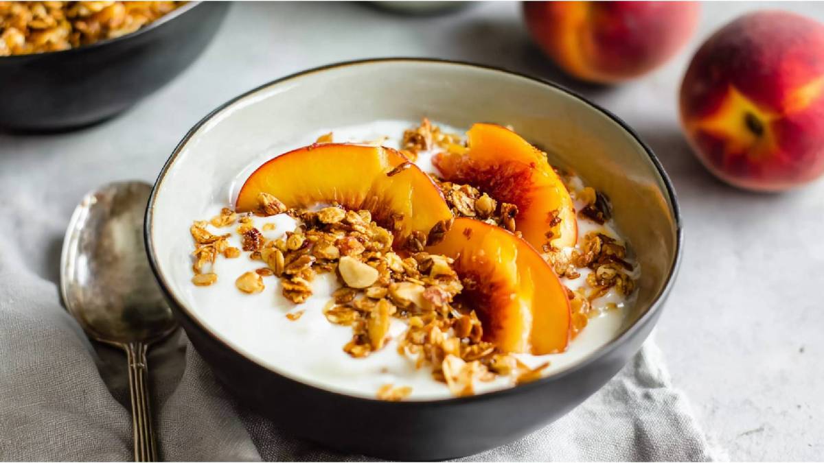 Kefir-Joghurt-Bowl mit gerösteten Pfirsichen auf einem Tisch, Pfirsiche im Hintergrund