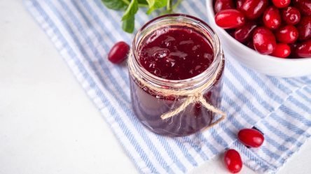 Ein Glas Kornelkirschen-Marmelade, daneben eine Schale mit Kornelkirschen.