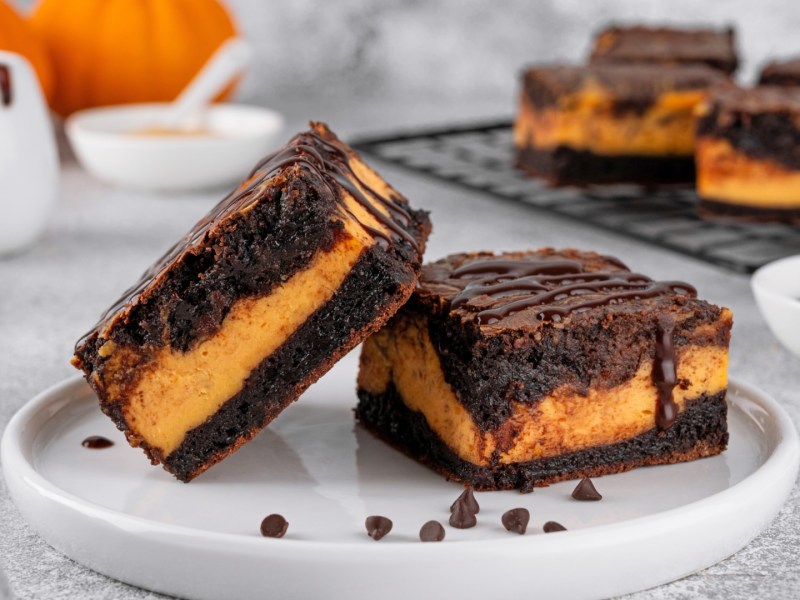 Zwei Kürbis-Cheesecake-Brownies auf einem Teller. Der Rest ist im Hintergrund zu sehen.
