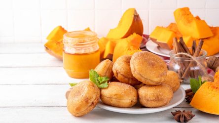 Ein Teller mit Kürbis-Krapfen aus dem Airfryer, dahinter einige Stücke Kürbis.