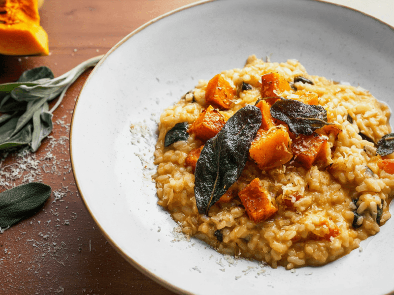 Ein Teller Kürbis-Salbei-Risotto, daneben Salbeiblätter und etwas Parmesan.
