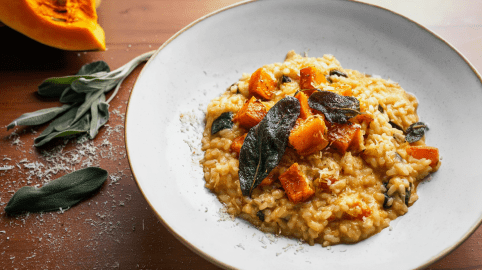 Ein Teller Kürbis-Salbei-Risotto, daneben Salbeiblätter und etwas Parmesan.