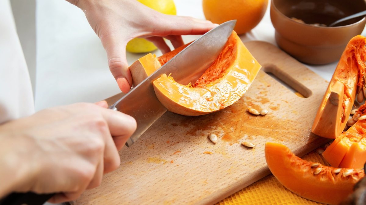 Kürbis schneiden: Eine Person halbiert ei Stück Kürbis.