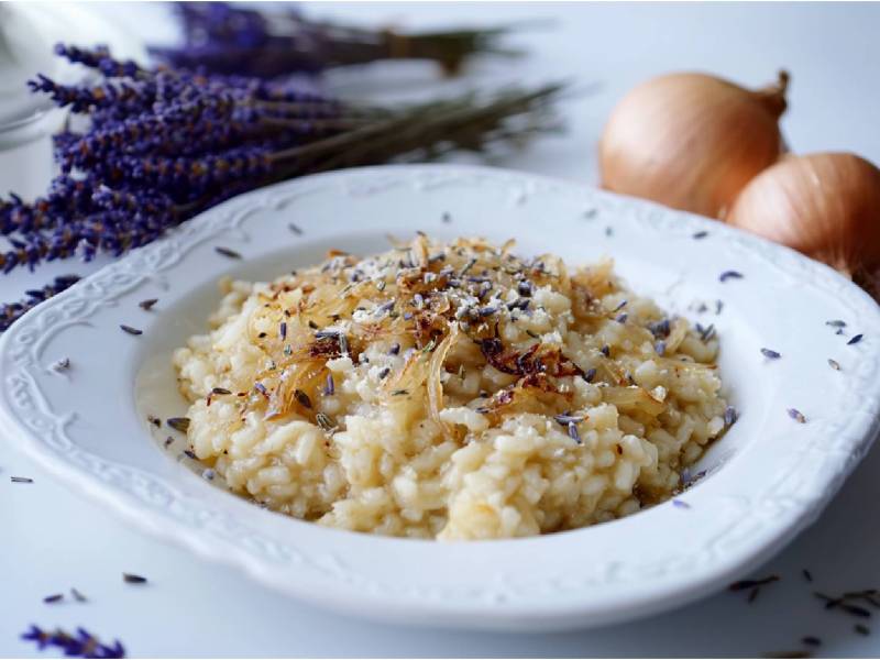 Teller mit Zwiebel-Lavendel-Risotto, Lavendelstrauß und Zwiebeln im Hintergrund