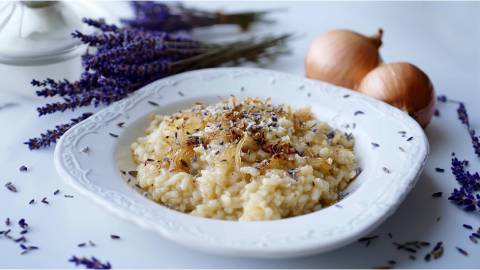 Teller mit Zwiebel-Lavendel-Risotto, Lavendelstrauß und Zwiebeln im Hintergrund