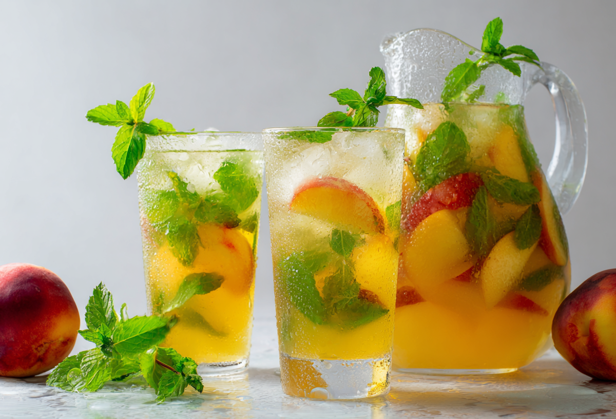 Zwei Gläser mit Nektarinen-Minz-Limonade. Daneben steht eine Glaskaraffe ebenfalls mit der Limo. Links und rechts im Bild liegen zwei Nektarinen. Vor den Gläsern liegt etwas Minze.