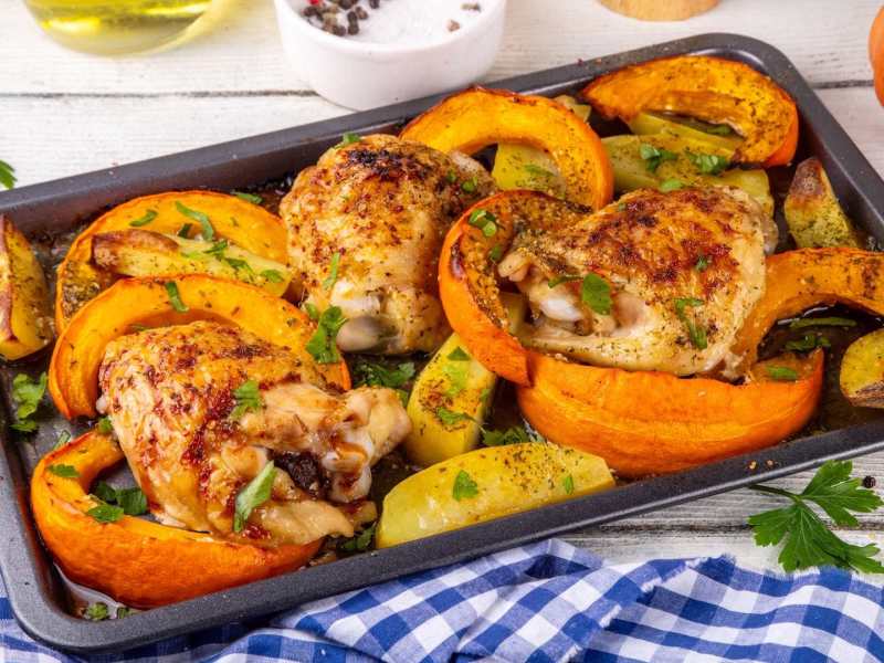 Ein Blech voll Ofenhähnchen mit Kürbis.