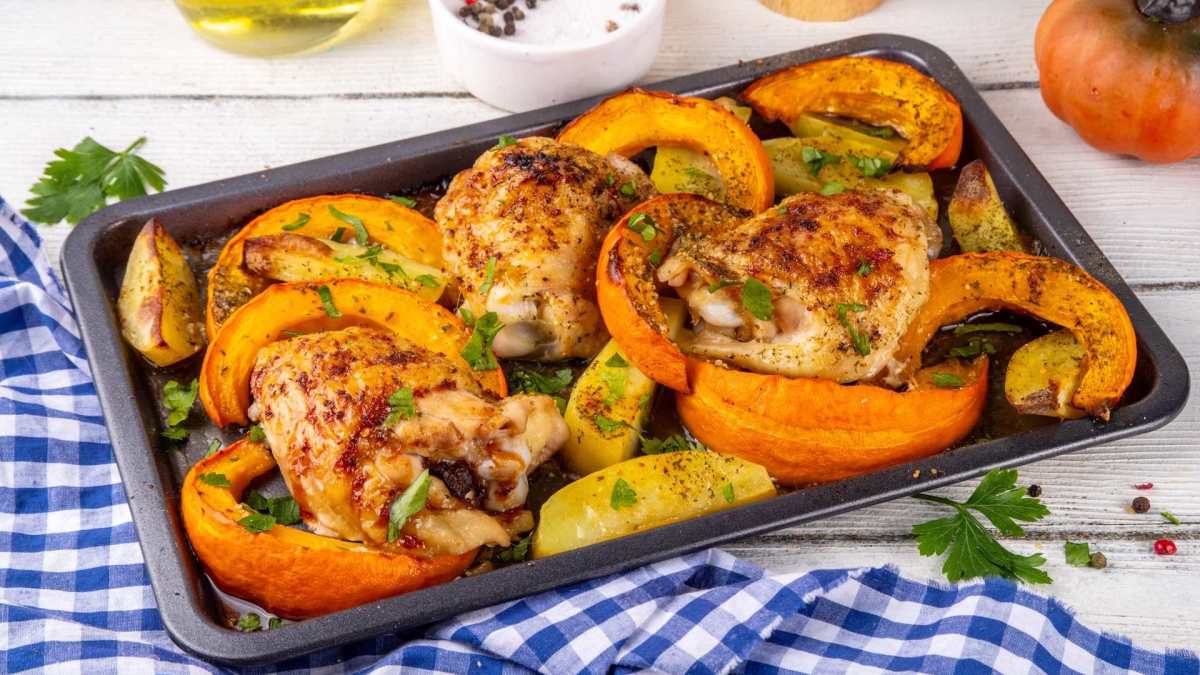 Ein Blech voll Ofenhähnchen mit Kürbis.