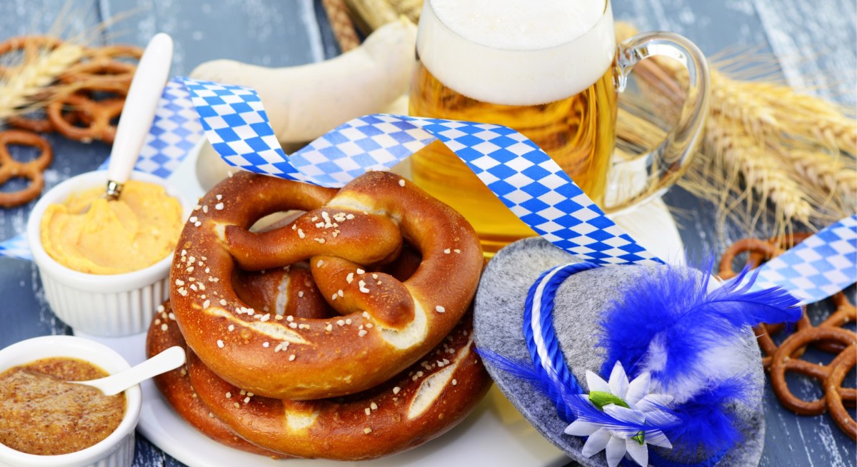 Brez'n, Obazda und weitere Oktoberfest-Klassiker liegen neben einer Maß Bier und einem typisch bayerischen Hut.
