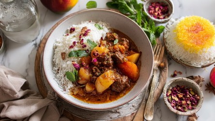 Ein Teller mit persischem Apfeleintopf. Ringsum ist persischer Reis, eine Schale mit getrockneten Rosenblättern sowie Gewürze zu sehen.