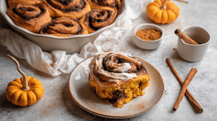 Pumpkin Spice Zimtschnecken in einer Backform, davor eine einzelne Zimtschnecke auf einem Teller.