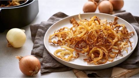 Schale mit Röstzwiebeln aus dem Airfryer, frische Zwiebeln und Airfryer im Hintergrund