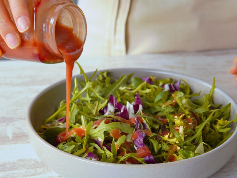 Jemad gießt Salatdressing aus Marmeladenresten über einen Salat.