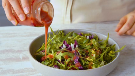 Jemad gießt Salatdressing aus Marmeladenresten über einen Salat.