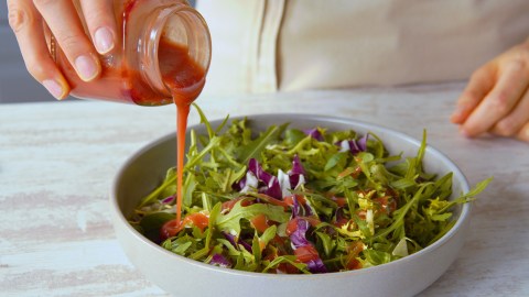 Jemad gießt Salatdressing aus Marmeladenresten über einen Salat.