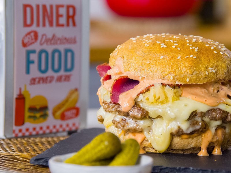 Ein Sauerkraut-Burger vor einem Serviettenspender, dazu Gewürzgurken.