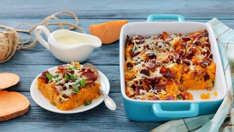 Süßkartoffelauflauf mit Pilzen, von dem bereits eine Portion entnommen wurde. Diese liegt auf einem Teller daneben.