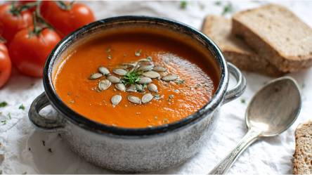Schale mit Tomaten-Kürbissuppe, Tomaten und Scheiben Brot daneben