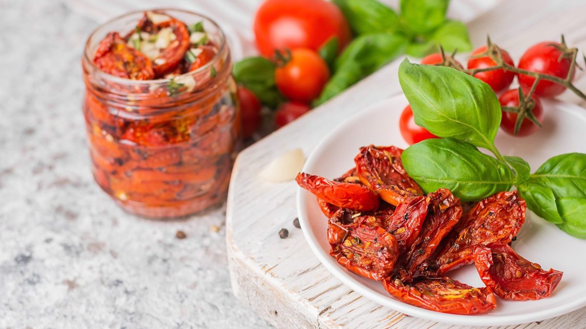Tomaten selbst trocknen: ein Teller getrocknete Tomaten, ein Glas Tomaten mit Öl im Hintergrund.