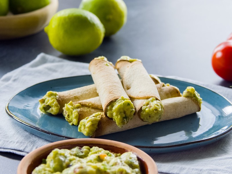 Mehrere Tortilla-Wraps mit Guacamole übereinander gestapelt auf einem Teller.