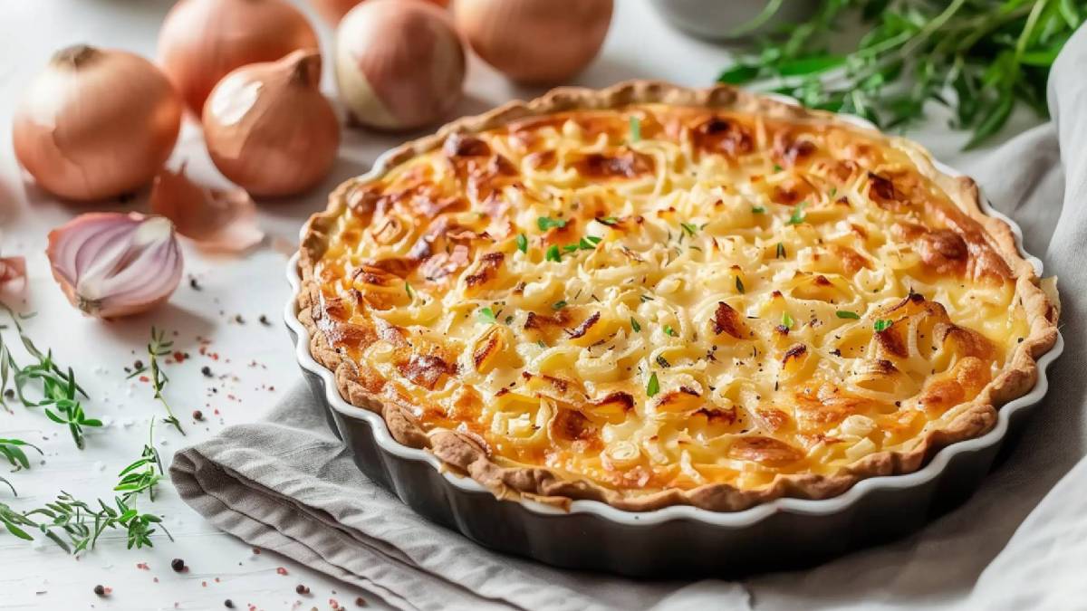 Veganer Zwiebelkuchen in einer Tarteform, frische Zwiebeln dahinter