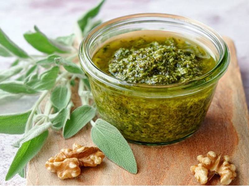 Ein Glas Walnuss-Salbei-Pesto mit frischem Salbei und Walnüssen daneben