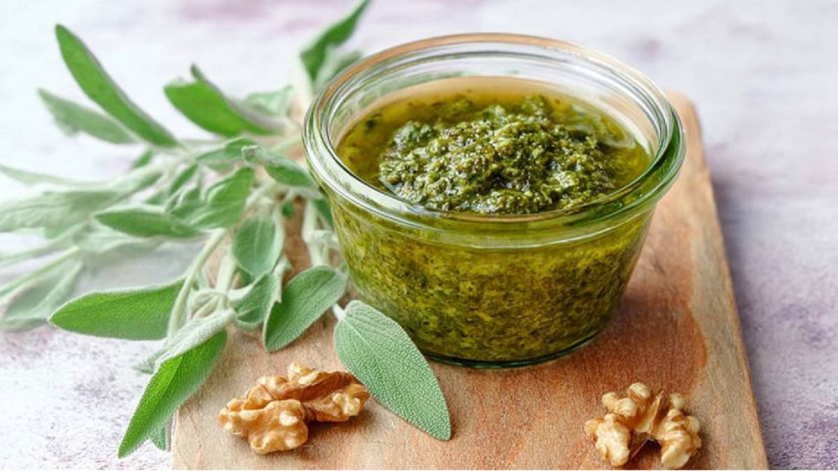 Ein Glas Walnuss-Salbei-Pesto mit frischem Salbei und Walnüssen daneben