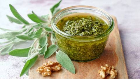 Ein Glas Walnuss-Salbei-Pesto mit frischem Salbei und Walnüssen daneben