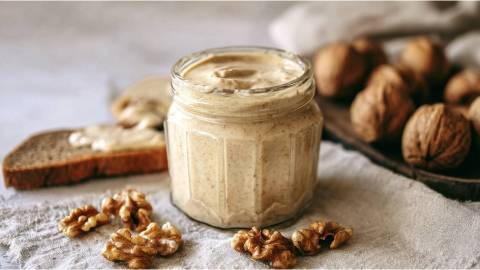 Ein Glas mit Walnussbutter und Walnüssen daneben