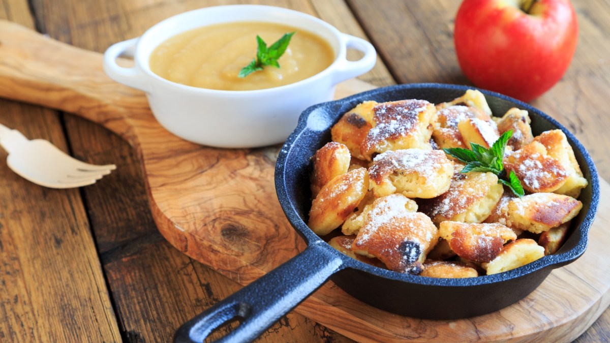 Apfelchmarrn in einer kleinen Pfanne. Daneben steht eine Schale mit Apfelmus und es liegt ein roter Apfel.