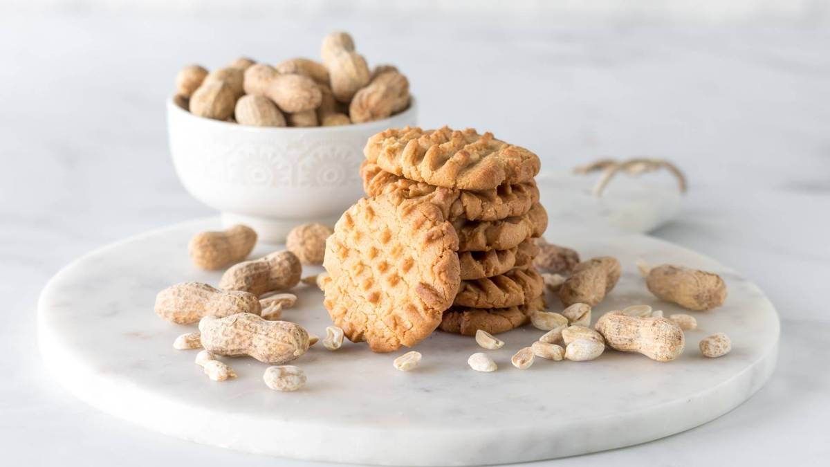 Ein Stapel mit Erdnussbutter-Miso-Cookies. Im Hintergrund steht eine Schüssel mit Erdnüssen.