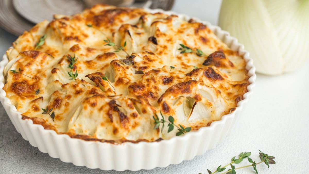 Eine Auflaufform mit Fenchelgratin, daneben eine Fenchelknolle.