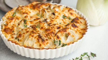 Eine Auflaufform mit Fenchelgratin, daneben eine Fenchelknolle.