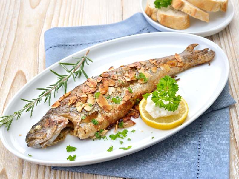 Forelle Müllerin-Art auf einem ovalen Teller, serviert mit Zitrone.