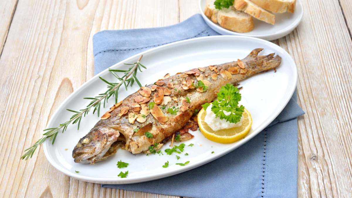 Forelle Müllerin-Art auf einem ovalen Teller, serviert mit Zitrone.