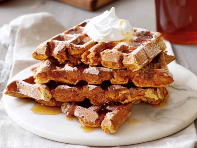 Mehrere French-Toast-Kürbis-Waffeln auf einem Teller übereinander gestapelt.