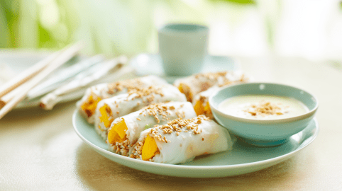 Ein Teller mit Frühlingsrollen mit Mango und Klebreis. Daneben steht eine Schale mit Dip.