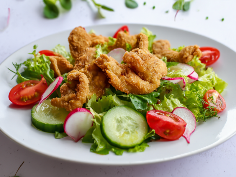 Ein Teller mit gebackenen Austernpilzen auf einem knackig-frischem Salat auf einem weißen Teller.